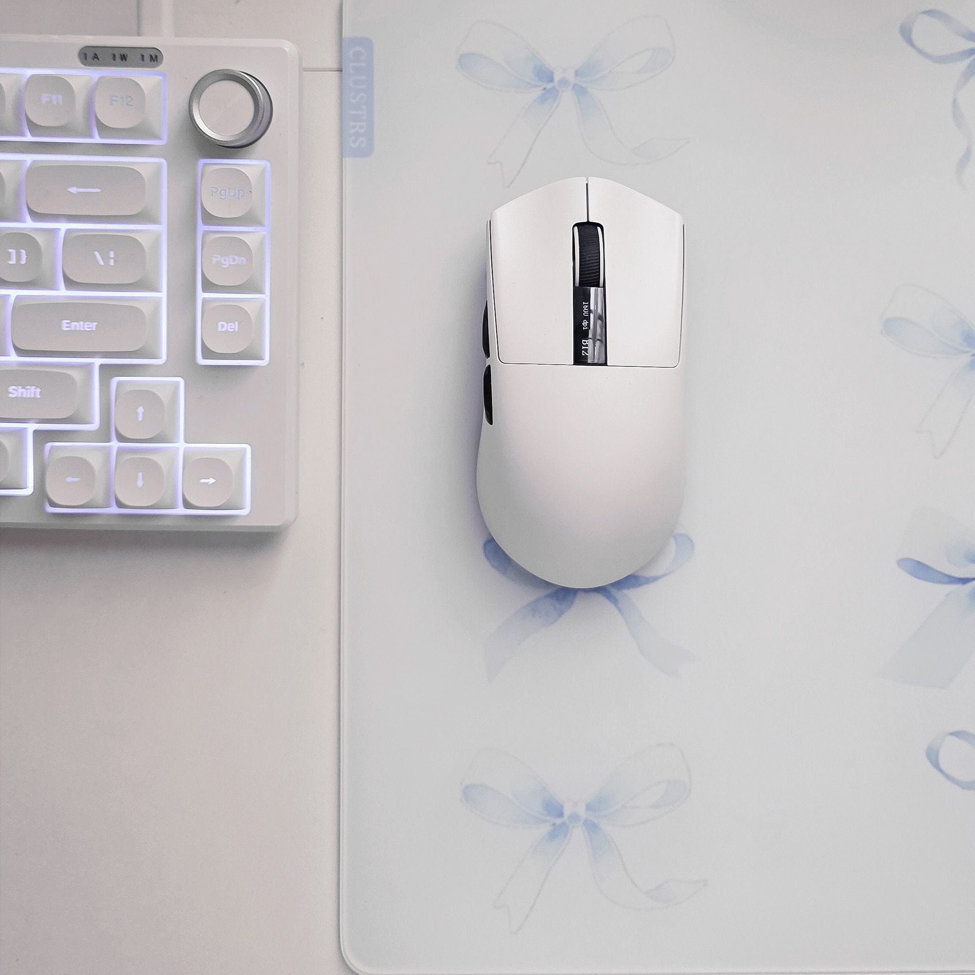 Close-up of the Blue Whisper glass mousepad with watercolor blue bows and a white gaming mouse.