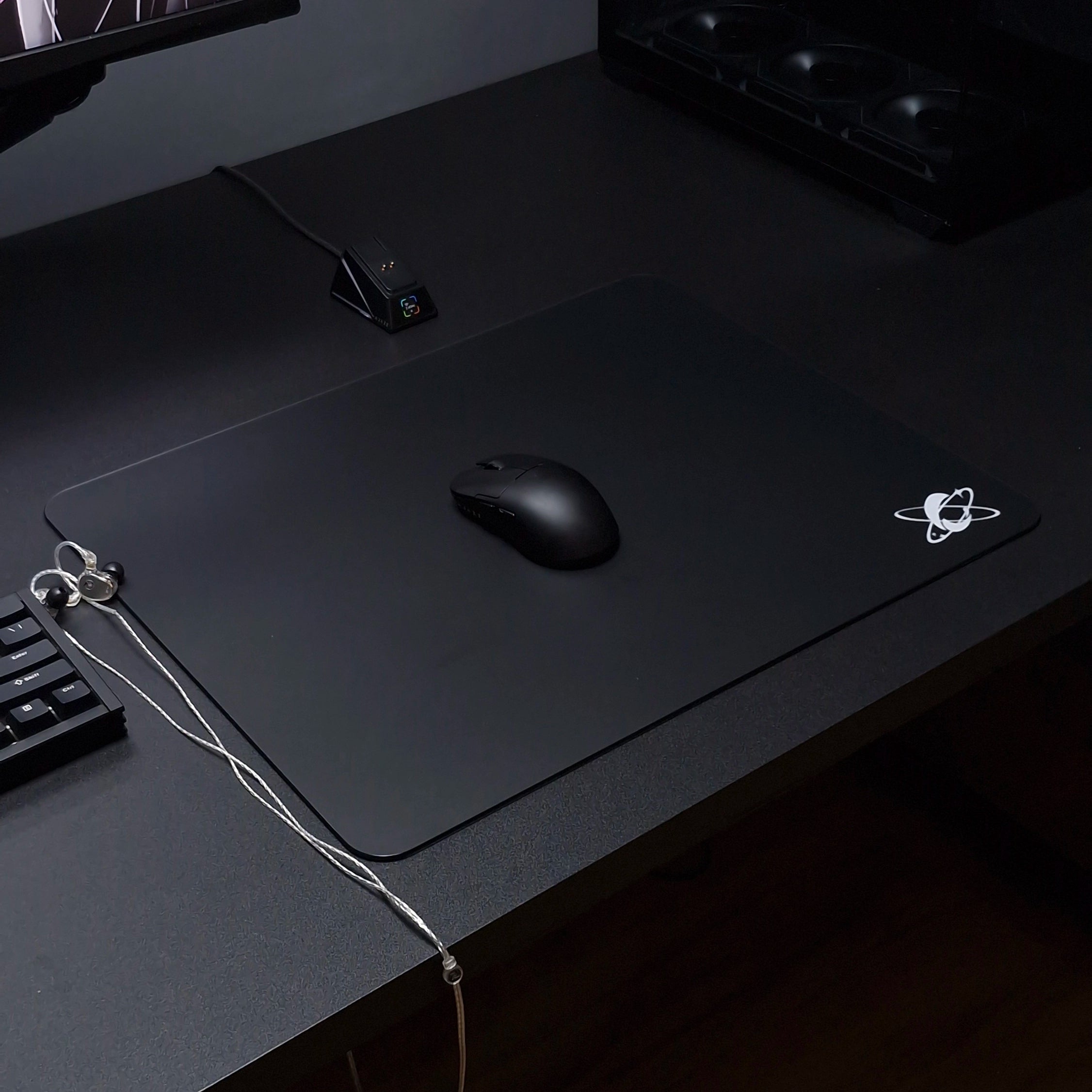 Minimal dark gaming desk setup featuring the Clustrs Atom Black Glass Pad Pro with a black wireless mouse on a smooth tempered glass surface.