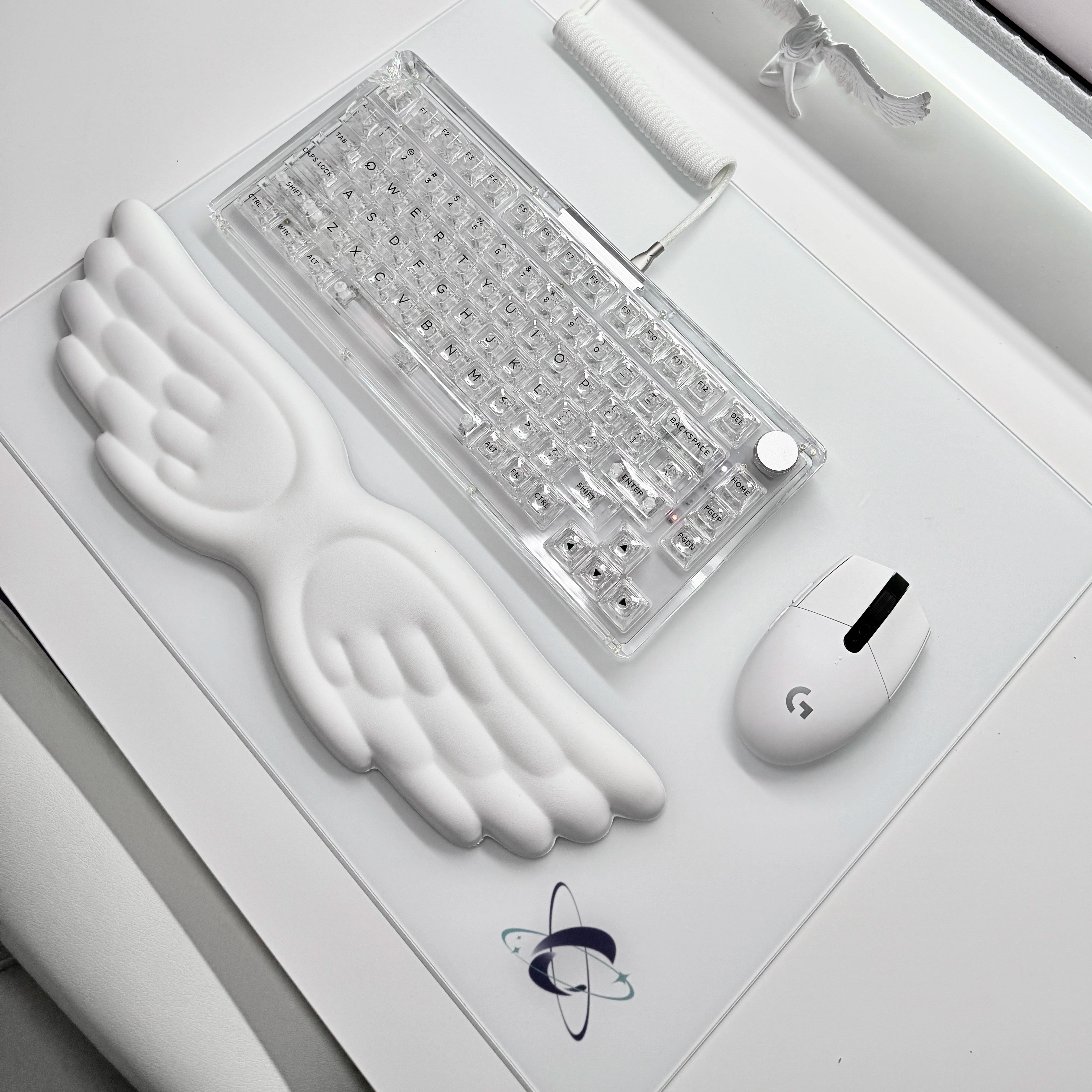 Aesthetic all-white desk setup featuring the Clustrs Atom White Glass Pad Pro with a transparent mechanical keyboard, wing-shaped wrist rest, and white Logitech mouse.