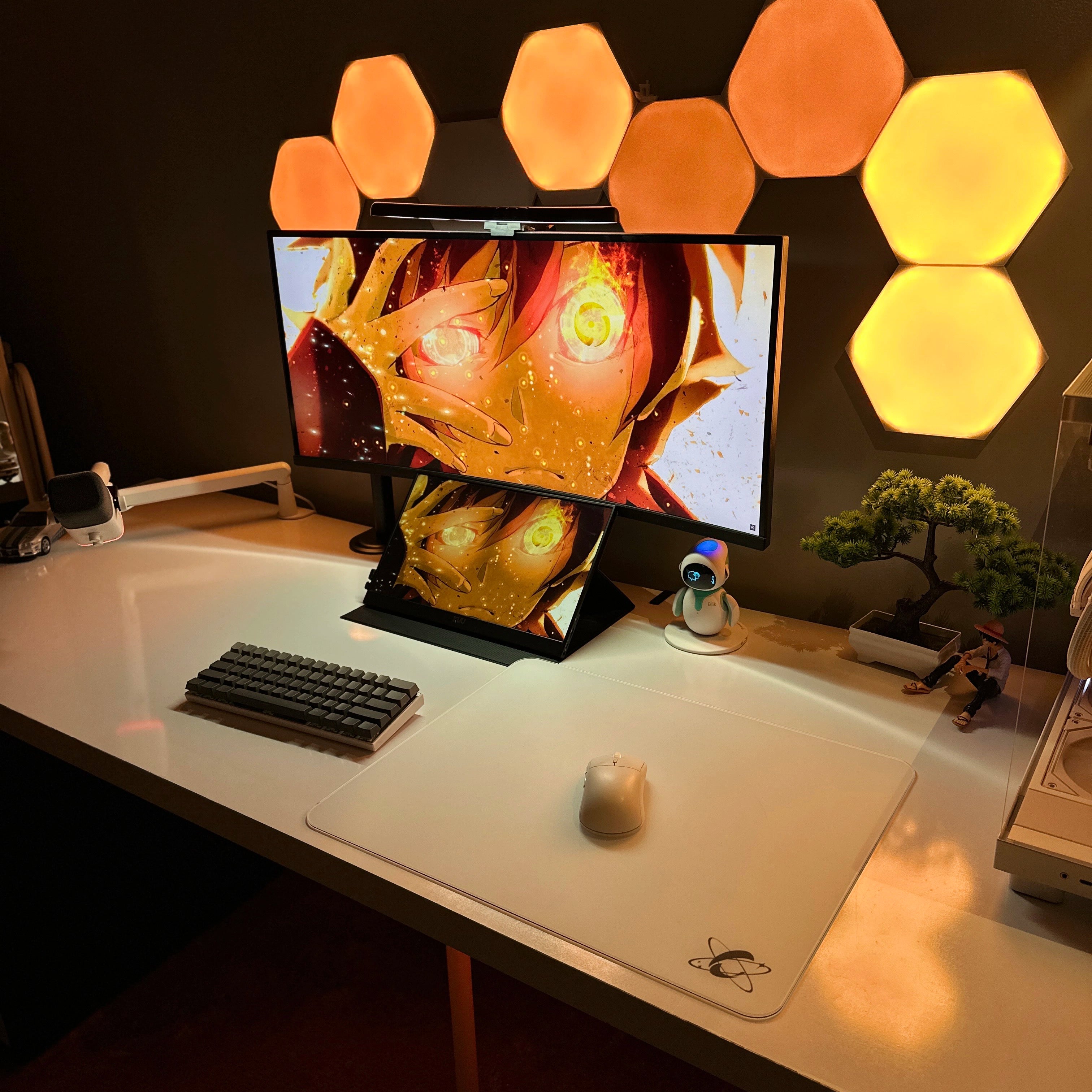 Warm RGB anime-themed desk setup featuring the Clustrs Atom White Glass Pad Pro with a white wireless mouse, compact mechanical keyboard, and dual displays.