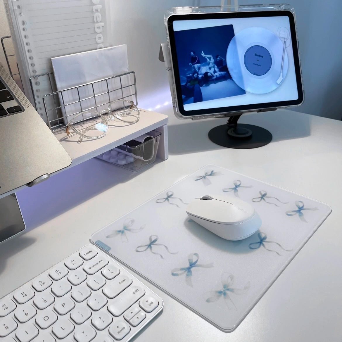 Clustrs Blue Whisper glass mousepad with blue ribbon pattern on a clean white aesthetic desk setup featuring a white wireless mouse, keyboard, and tablet.