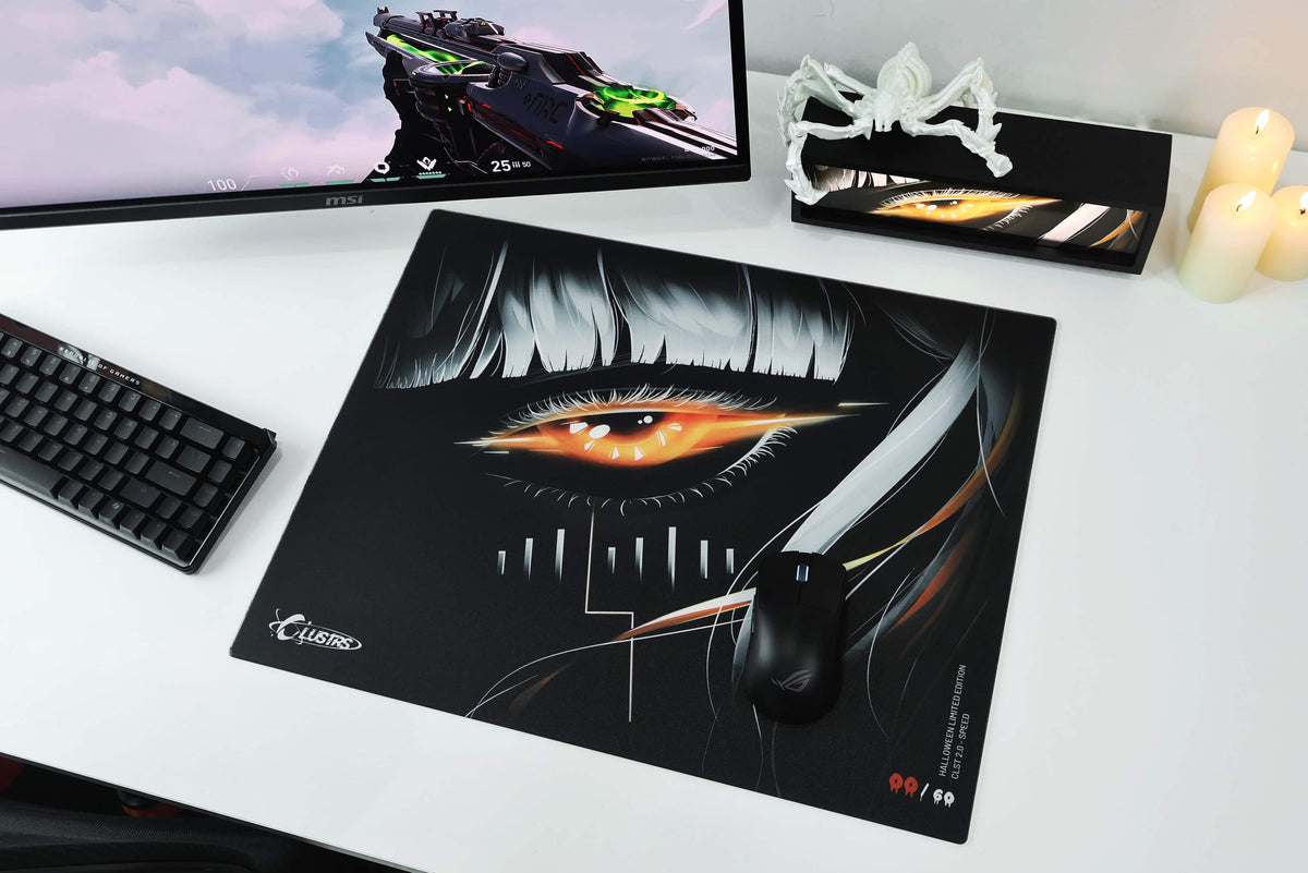 EMBER Halloween glass mousepad with glowing orange eye artwork on a white gaming desk setup with a keyboard, monitor, and mouse.
