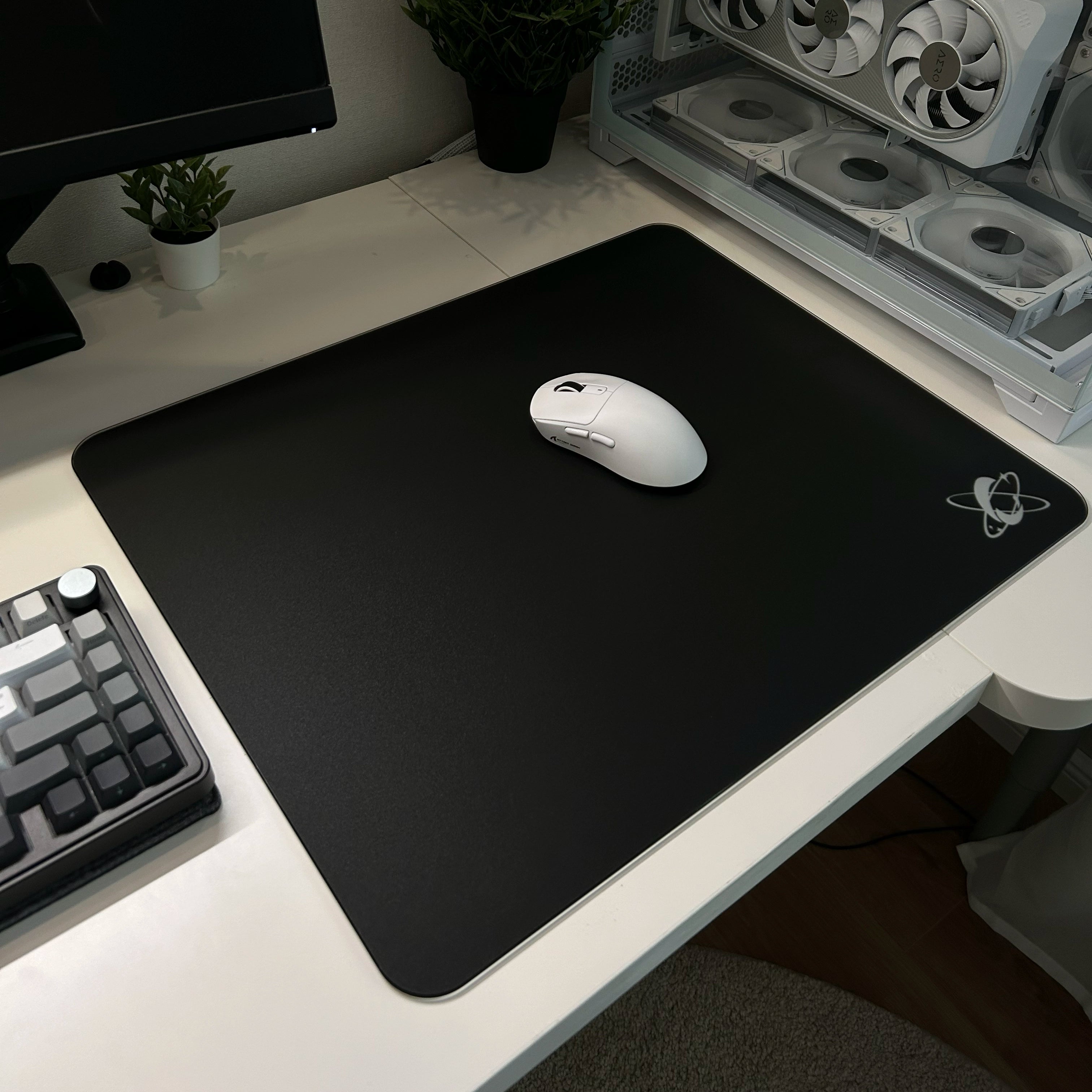 Clustrs Atom Black Glass Pad Pro on a clean white desk setup with a wireless mouse, showcasing the ultra-smooth tempered glass surface for gaming and productivity.