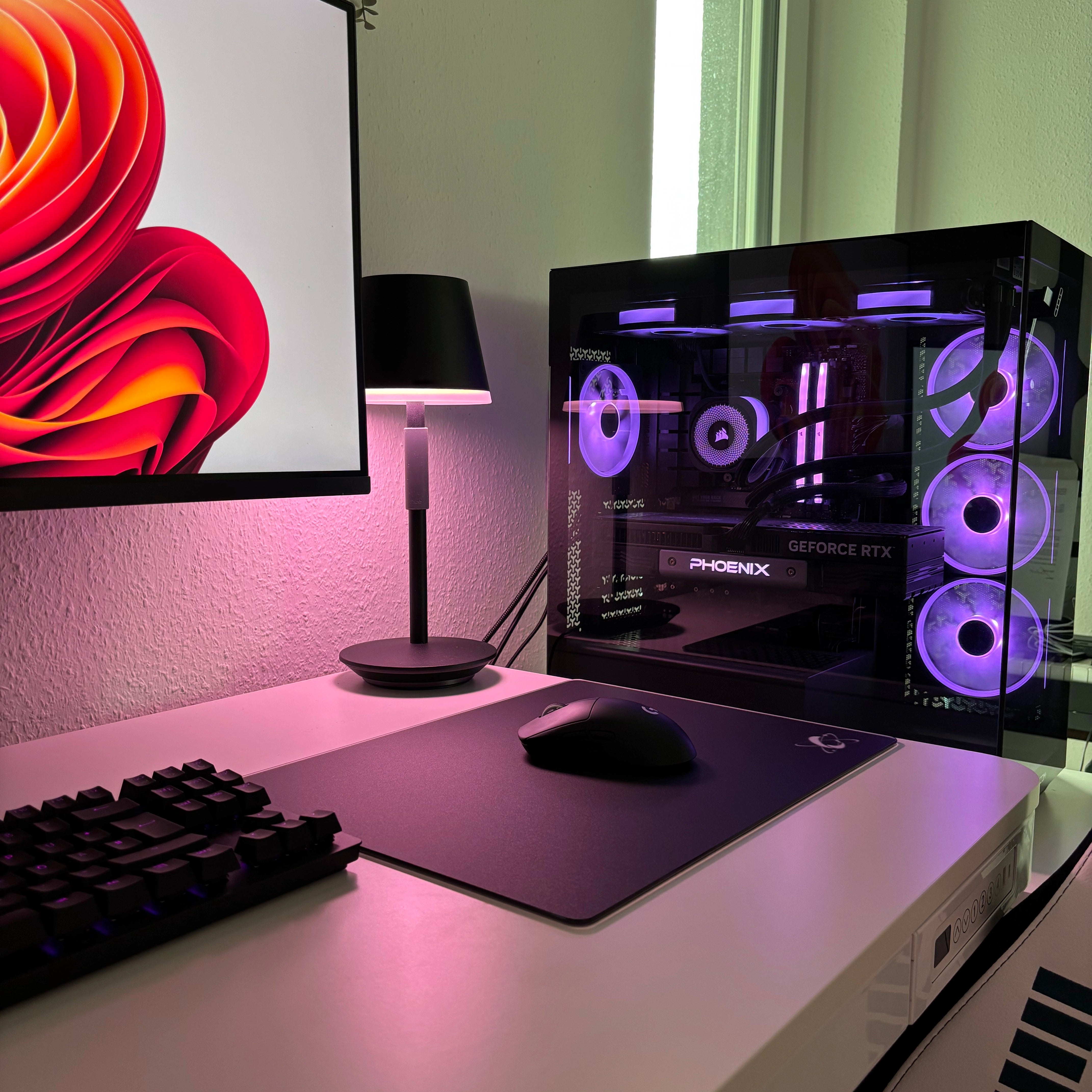 Purple RGB gaming desk setup featuring the Clustrs Atom Black Glass Pad Pro with a wireless mouse next to a PC tower with illuminated fans.