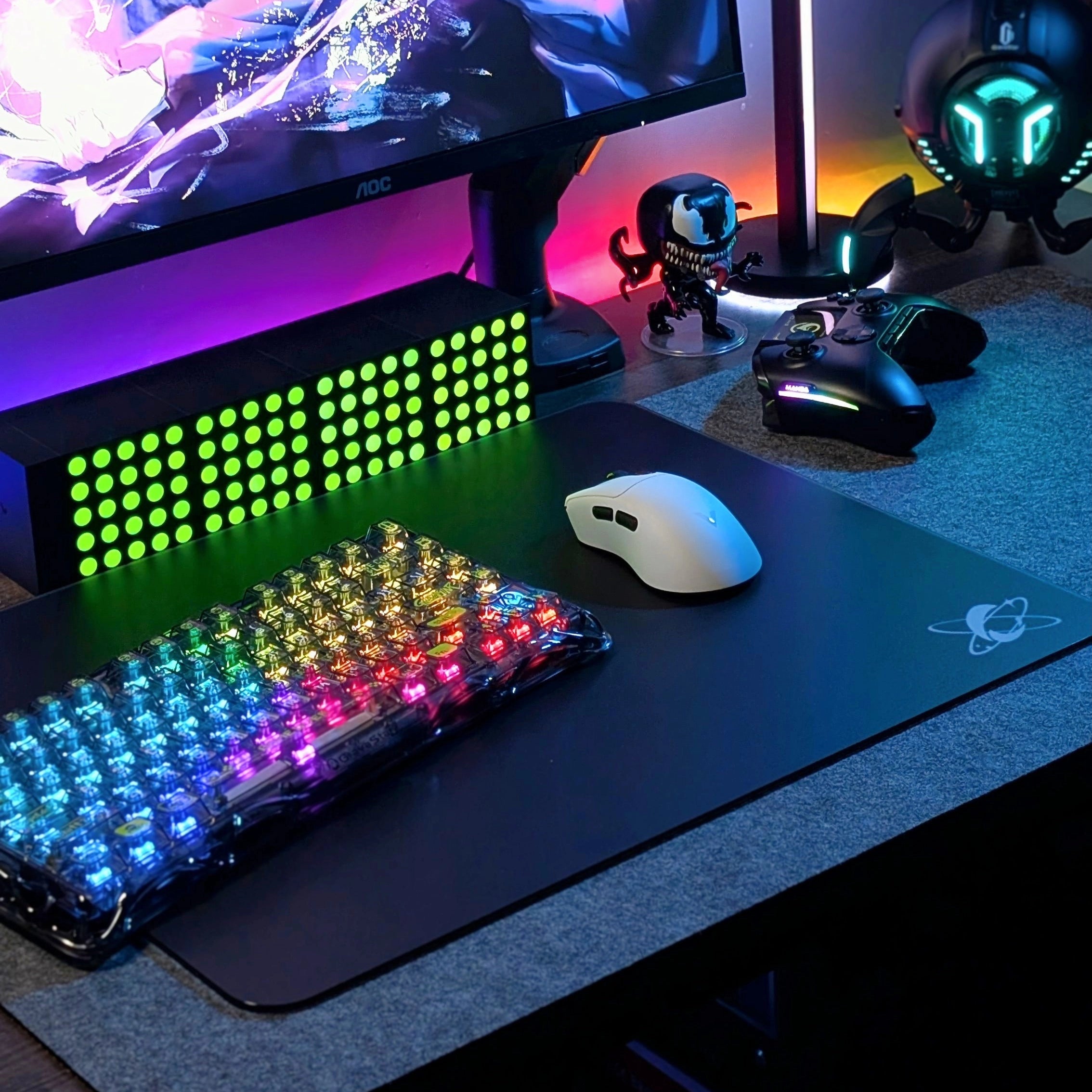 RGB gaming desk setup featuring the Clustrs Atom Black Glass Pad Pro with a transparent mechanical keyboard and wireless mouse on a sleek tempered glass surface.