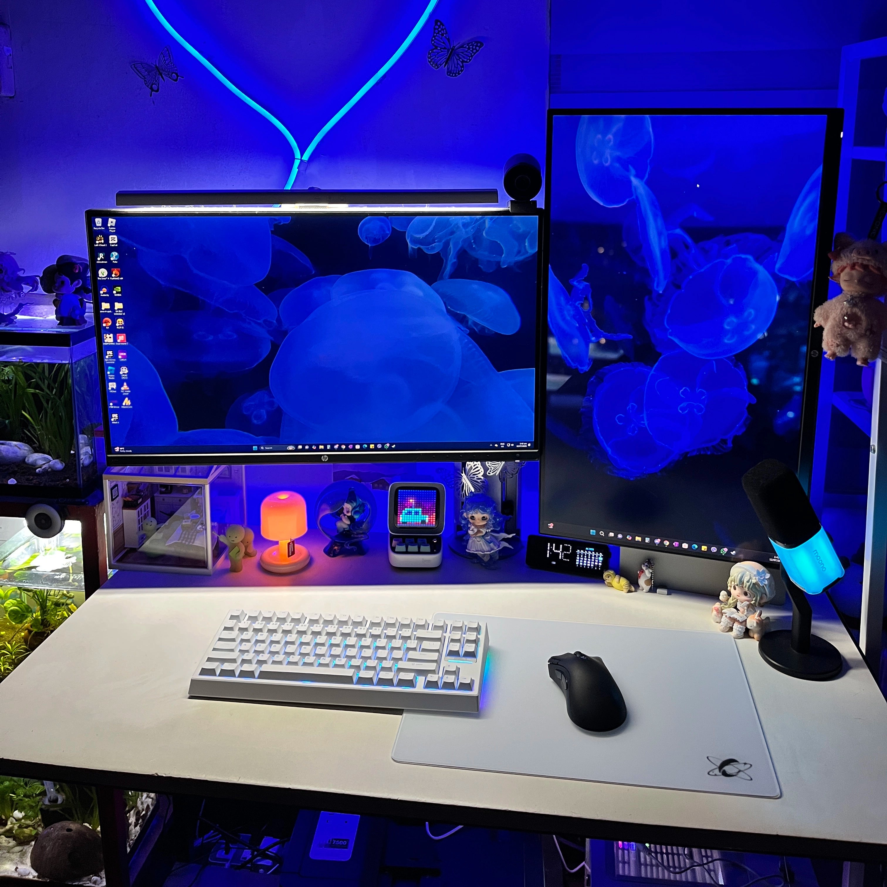 Blue RGB gaming desk setup featuring the Clustrs Atom White Glass Pad Pro with a white mechanical keyboard, black wireless mouse, and dual monitors.
